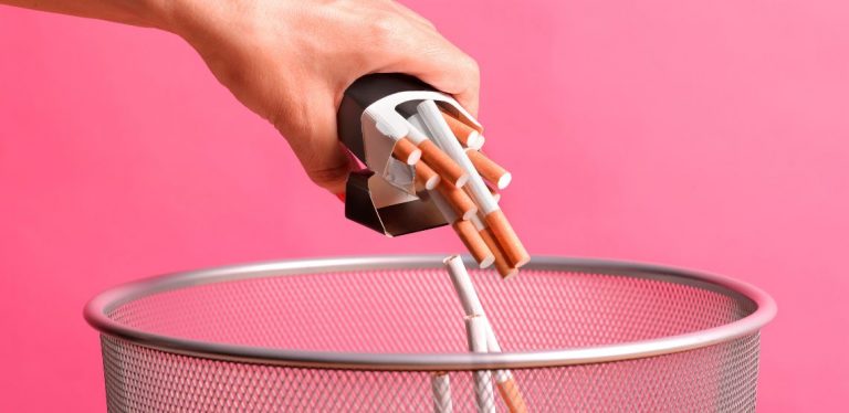 A person throwing cigarettes into a garbage can.