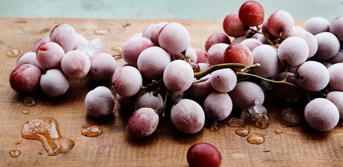 A bunch of frozen red grapes sitting on a brown cutting board.