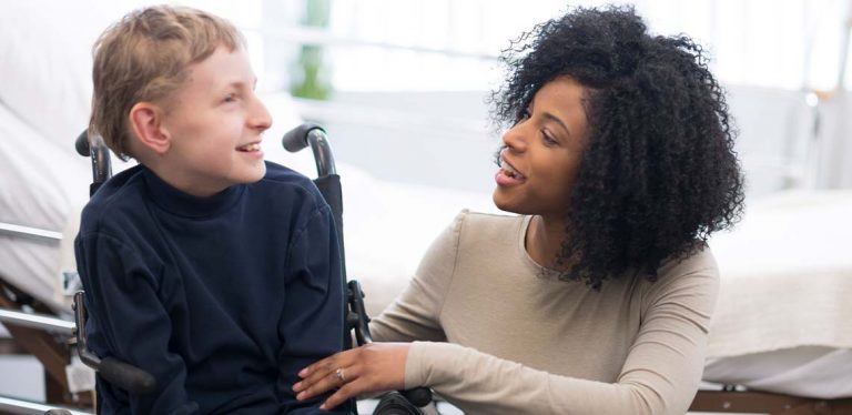 a boy with cerebral palsy sitting in a wheelchair talking to a lady.