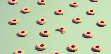 Rows of cookies with one in the middle having a bite out of it against a light green background.
